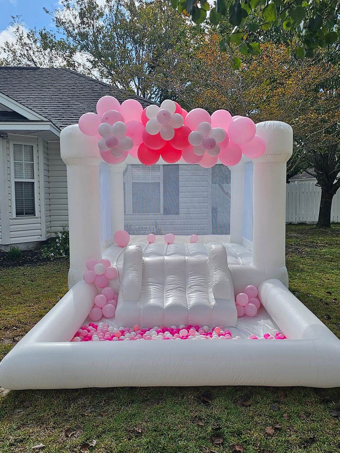 White bounce house styled with pink balloons for a backyard party